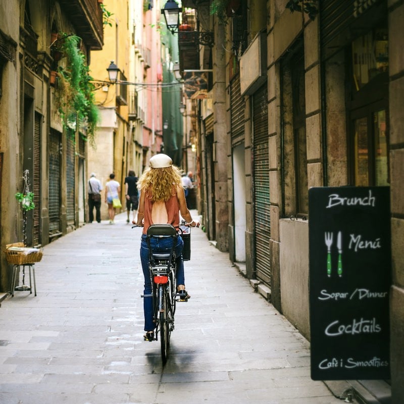 Woman riding bicycle through old street of Barcelona