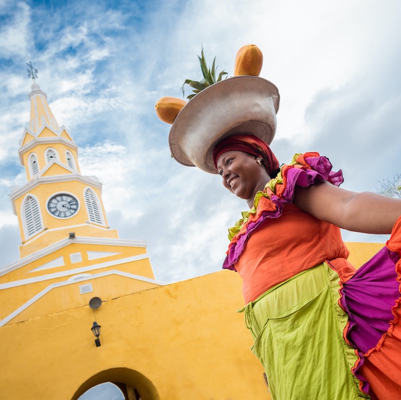 Happy Palenquera selling fruits in Cartagena with yellow colonial building in the background