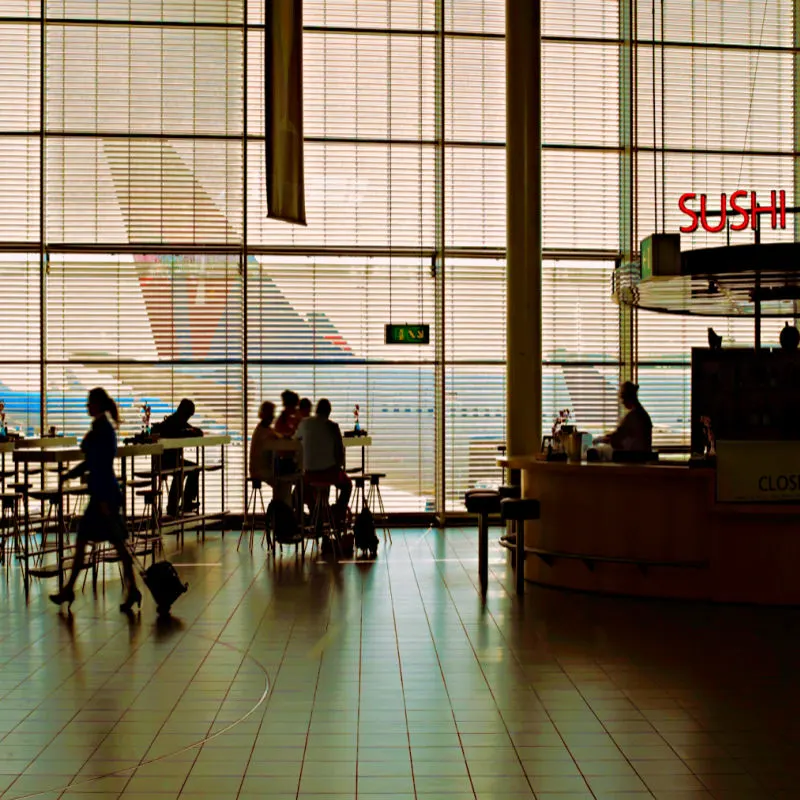 Airport interior with food bar and tourists.