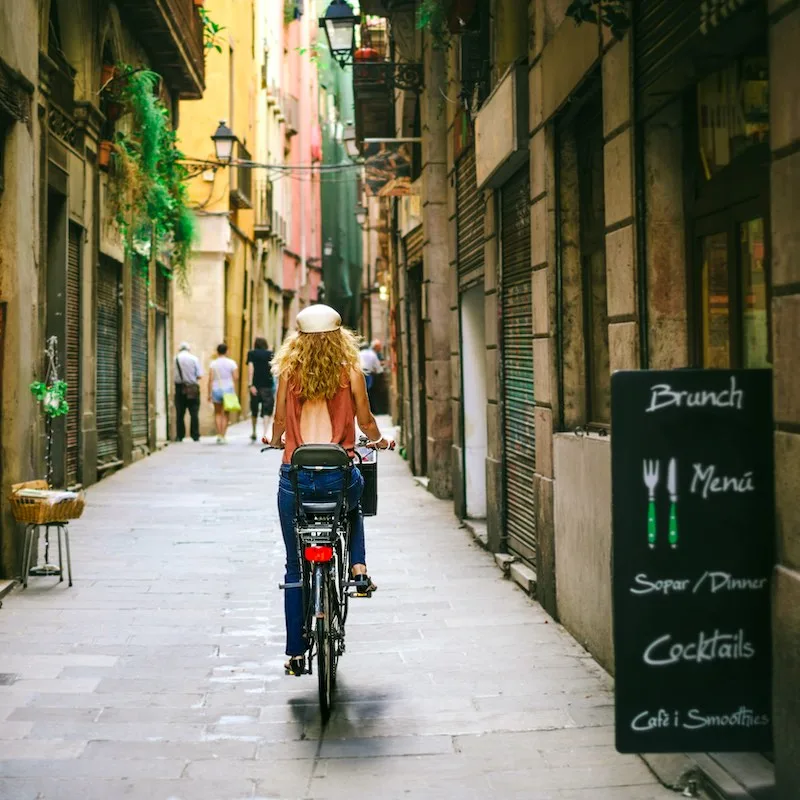 Woman riding bicycle through old street of Barcelona