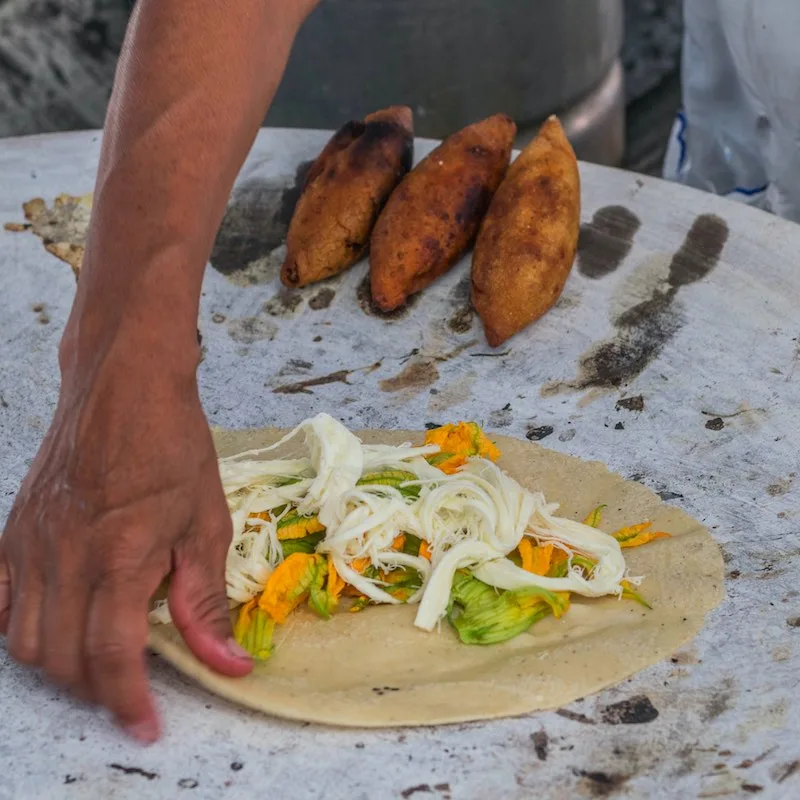 Oaxaca, Mexico- July 18, 2018: a Mexican woman preparing a squash blossom quesadilla on a large comal