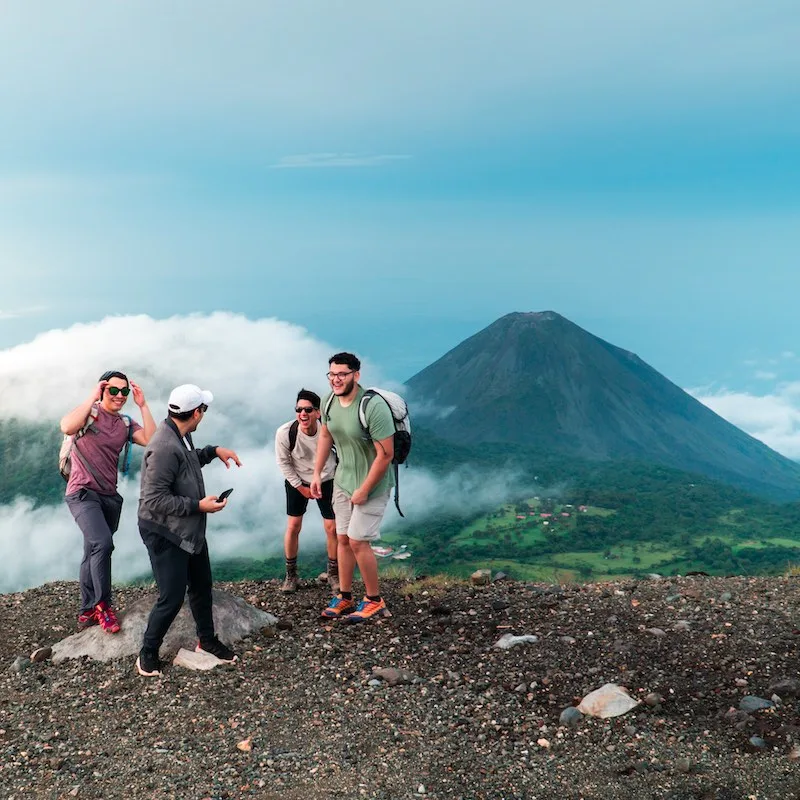 latin tourists have fun on top of a mountain with the El Salvador Volcano at the background